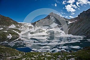 Lake sits nestled amidst snow covered mountains under a clear blue sky