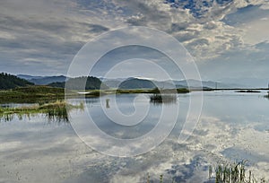 lake with sky reflection and reeds surrounded by mountains