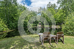 Lake surrounded by greenery with two Adirondack chairs facing the lake in the daytime