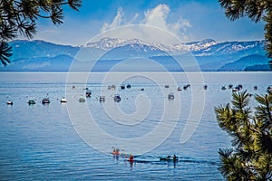 Lake Tahoe with turqoise blue sater and many boats moored and tourists paddleboating with snowcovered mountains in distance framed