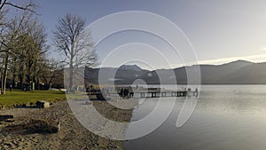 Lake Tegernsee, Bavaria, Germany. People relaxing on sunny spring day on lakeside beach and pier overlooking Bavarian