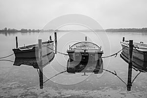 a lake there are several rowing boats on the shore and they are chained and the water is mirror-smooth