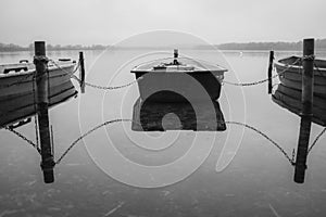 a lake there are several rowing boats on the shore and they are chained and the water is mirror-smooth