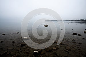 Lakeshore view on a foggy winter day - fog, frost and snow cover the lakeside of the famous lake â€žChiemseeâ€œ in Bavaria,