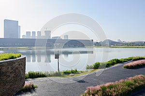 Lakeside asphalted path in summer morning with modern buildings across lake