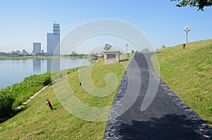 Lakeside blacktopped pedestrian way on grassy slope in morning with modern buildings in distance photo