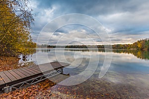 Lakeside with jetty, fallen leaves and treeline in bright autumn colors