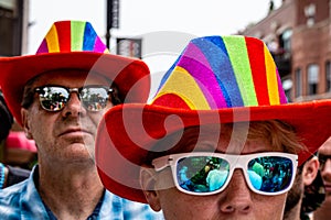 A woman and man are wearing sunglasses and matching rainbow hats to show LGBTQ support at Gay Pride