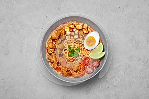 Laksa in gray bowl on concrete table top. Coconut noodle soup with chicken meat and prawns of peranakan cuisine