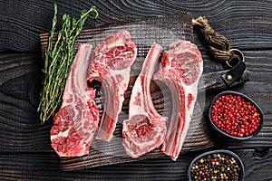 Lamb chops raw meat on bone with salt, pepper and herbs. Black wooden background. Top view