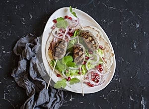 Lamb kebab on flatbread with lettuce, onions and pomegranate. On a dark background