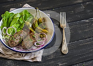 Lamb kebab, spicy roasted peppers and fresh green salad on the plate on a dark wooden surface