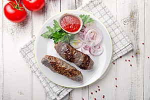 Lamb Lula kebab with greens and sliced red onion and tomato sause on white wooden table