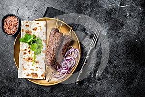 Lamb meat kofta kebab, onion and flat bread on plate. Black background. Top view. Copy space