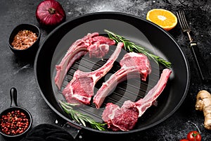 Lamb rib cuts cutlet, on frying cast iron pan, on black dark stone table background