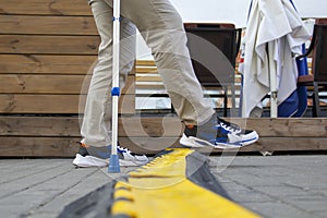 A lame man with an elbow crutch steps over a cable channel in the street.