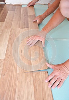 Laminate flooring installation. Men are installing plastic laminate flooring over a vapor blue underlayment