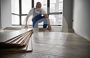 Laminate planks and male flooring installer on background.