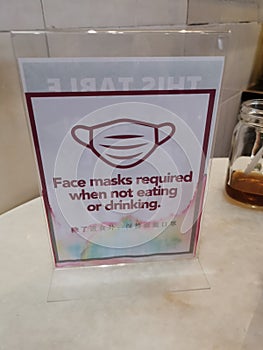 Laminated table signboard which English wording of `face masks required when not eating or drinking` with mandarin words interpret