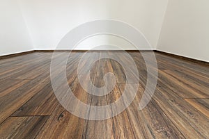 Laminated wood floor with white wall. Empty room with floating laminate in new apartmen