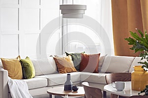 Lamp above table in bright living room interior with yellow pillows on white corner sofa. Real photo