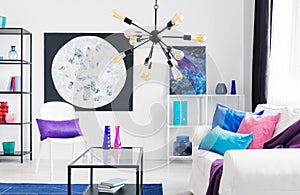 Lamp above table and white couch with pink and blue pillows in loft interior with posters. Real photo