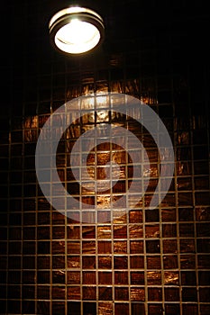 Lamp on the background of brown shiny wall with ceramic mosaic tiles