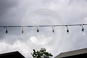 A lamp bulb on the wires, on background of a sky before raining