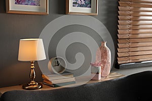 Lamp, clock, books and decor elements on table in living room. Interior design