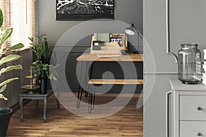 Lamp and organiser on wooden desk in grey home office interior with black poster. Real photo