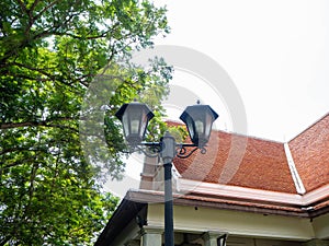 Lamp post in garden color black,Behind orange gable roof,Sky clean and clear,At Sri Nakhon Khuean Khan Park and Botanical Garden i