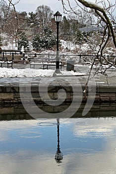 lamp post street light and its reflection in the pond at prospect park brooklyn new york city in winter with snow