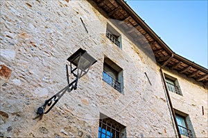 Lamp for public lighting and stone wall windows in a historic building in the medieval village of Strassoldo.