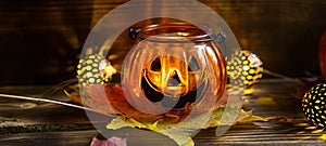 Lamp pumpkin with eyes and mouth made of glass and natural orange pumpkin on a wooden table with yellow and red maple leaves. Hall