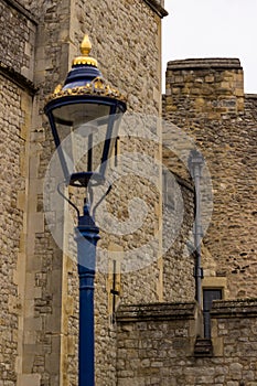 A lamp stands out in gold and blue splendor against dull stonework of medieval fortifications.