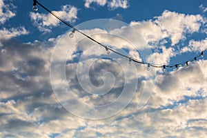 Lamp string hanging against a cloudy blue sky background