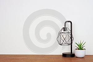 Lamp and succulent plant home decor on a wood shelf against a white wall with copy space.