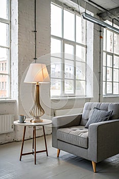 Lamp on table next to grey settee in white loft interior