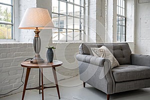 Lamp on table next to grey settee in white loft interior