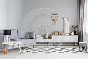 Lamp on table next to grey sofa in scandi living room interior w