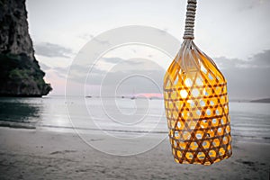 The lamp on the wire tied with a rope. On the background of the beach, mountain and sunset. Inside the light bulb shines, evening