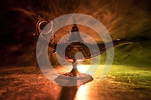 Lamp of wishes concept. Antique Aladdin arabian nights genie style oil lamp with soft light white smoke, Dark background