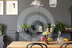 Lamps above wooden table and black chairs in grey dining room in