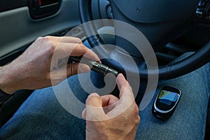 Lancet pen and glucometer in the hands of a man in a car. Diabetes concept
