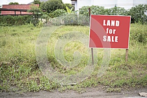 Land for sale sign. Red sign for sale plot. Green lawn behind sign. Land for sale signboard on street signs