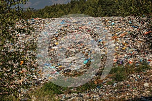 Landfill / dump site surrounded by green trees and mountains in background no logos / trademarks visible on dumped garbage