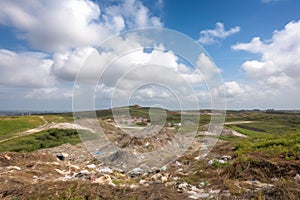 landfill surrounded by lush natural landscape, with clear blue skies and fluffy clouds in the background