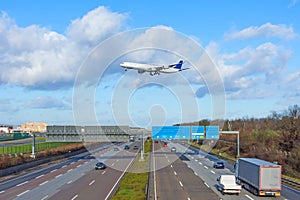 Landing airplane flies over a high-speed highway with cars in the city. Travel concept by air or ground