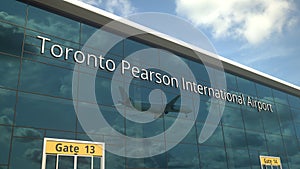 Landing airplane reflects in the modern windows with Toronto Pearson International Airport text