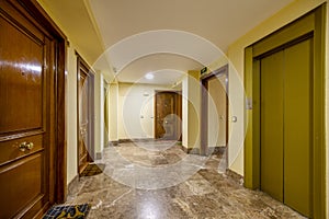 Landing of a residential apartment building with brown marble floors and ocher green metal elevator